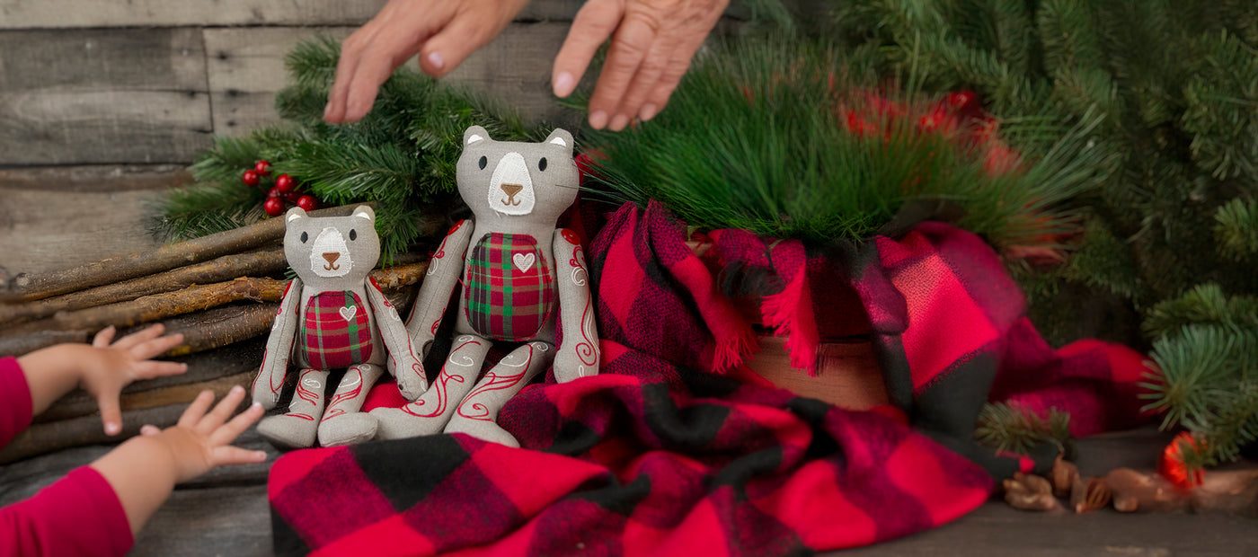 Two machine embroidered teddy bears with plaid patches on a red and black checkered blanket with Christmas decorations.