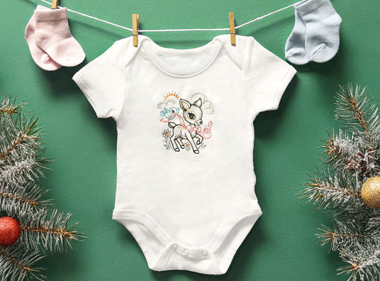 White baby onesie with a deer design on a green background with Christmas decorations.