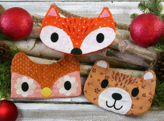 Machine embroidered animal zipper pouches - fox, owl and bear resting on wooden sticks surrounded by red ornaments.