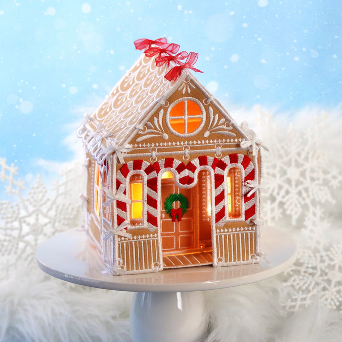 Machine embroidered 3D gingerbread house on a cake topper with a blue and snowflake background