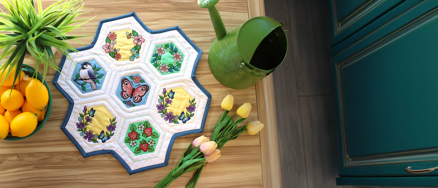 Machine embroidery hexagon quilt spring designs on a wooden table surrounded by flowers, lemons and a watering can. 