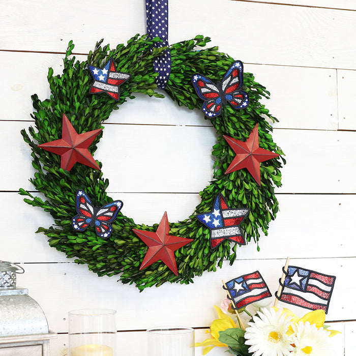Machine embroidered patriotic lace designs staged on a green wreath, hanging on a white wood wall.