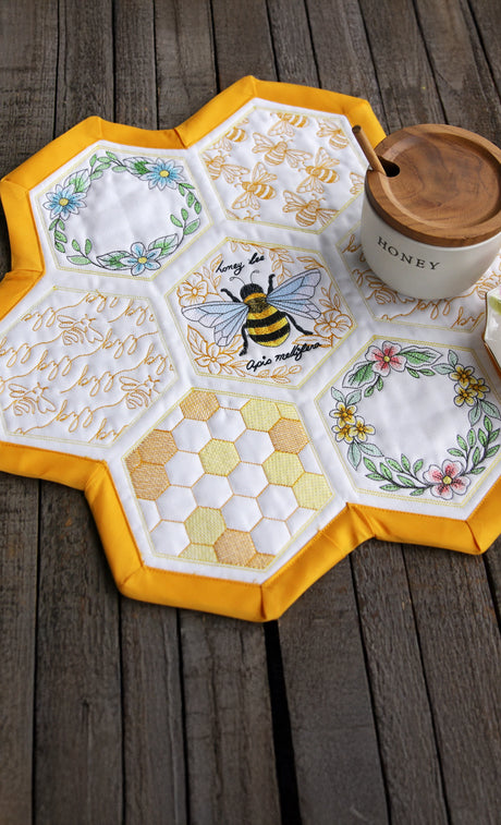 Machine embroidery hexagon quilt tabletop set with bee and honeycomb designs on a wooden surface.