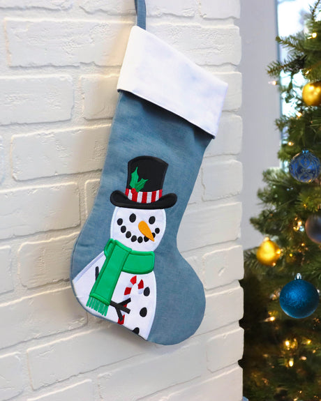 Machine embroidery applique snowman design on stocking hanging on a white brick wall.