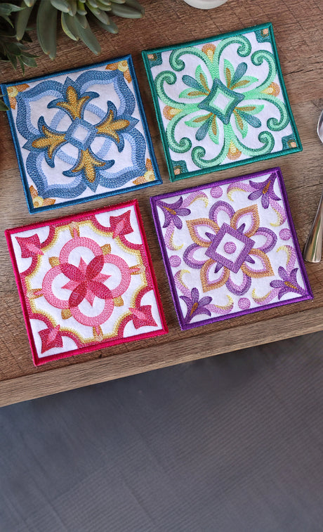Four colorful machine embroidery in-the-hoop coasters on a wooden table.
