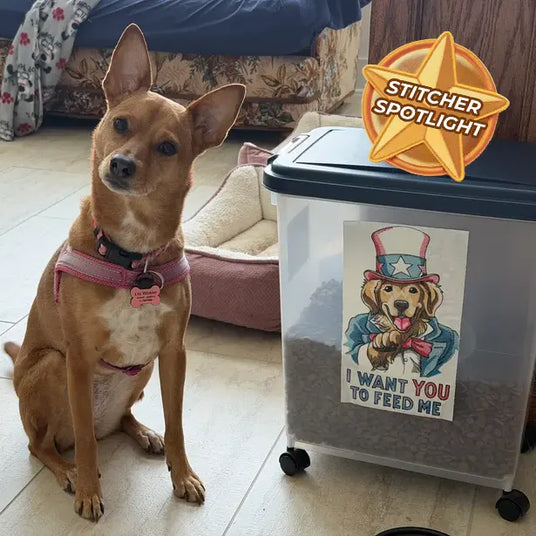 Customer dog sitting beside a rolling pet food container decorated with a machine embroidered patriotic dog design reading “I Want You to Feed Me,” with a Stitcher Spotlight badge in the corner.