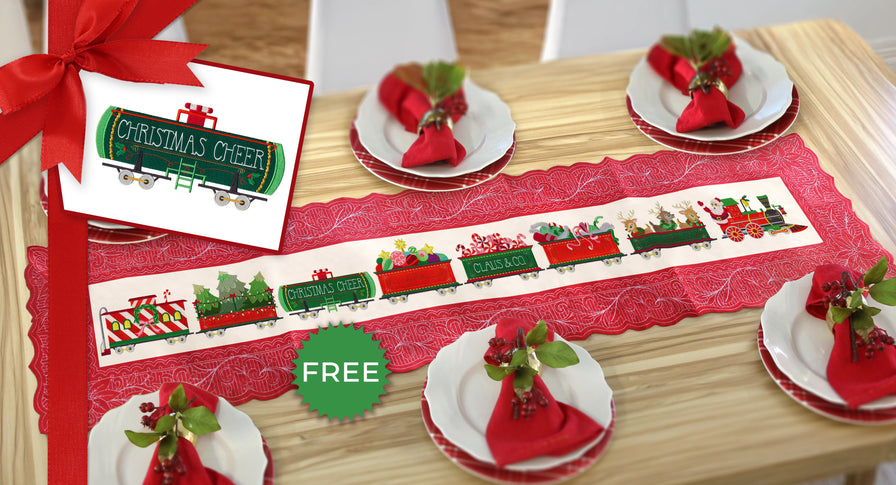 Christmas-themed table setting with a quilted red tablecloth featuring machine embroidered train designs, and festive napkins on a wooden table.