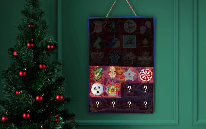 A hanging  machine embroidered Christmas advent calendar with colorful illustrated compartments and question marks, displayed against a dark green paneled wall next to a decorated Christmas tree.