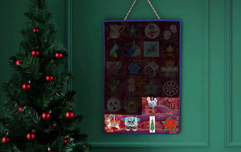 A Christmas advent calendar hanging on a dark green paneled wall next to a decorated Christmas tree. The calendar has multiple colorful pockets and compartments with various festive machine embroidered ornaments, including Santa Claus, reindeer, ornaments, and gifts.