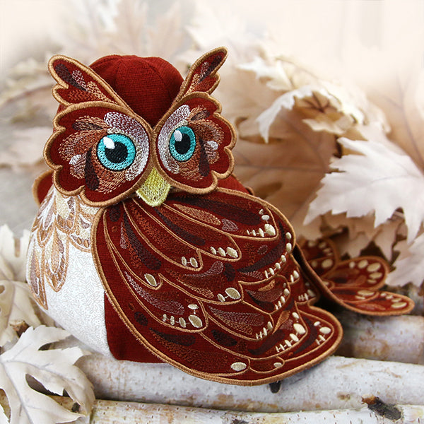 3D embroidered owl stuffie with turquoise eyes, shown perched on birch logs and surrounded by fall leaves.