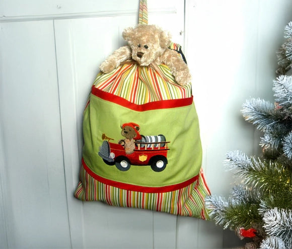 Decorative machine embroidered bag with a teddy bear and fire truck design, hanging on a white door.